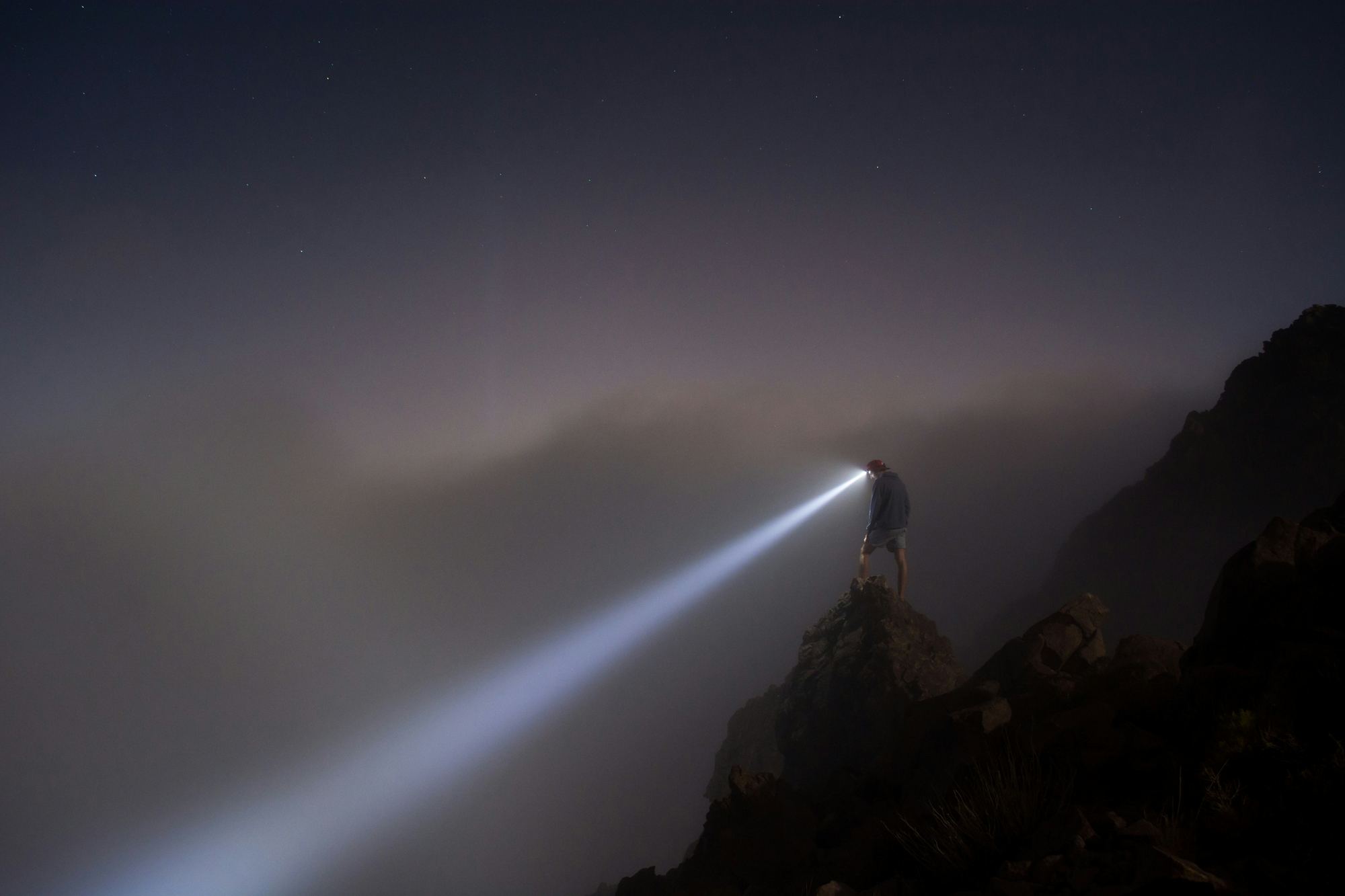 Headlamp beam cutting through darkness on a mountain trail